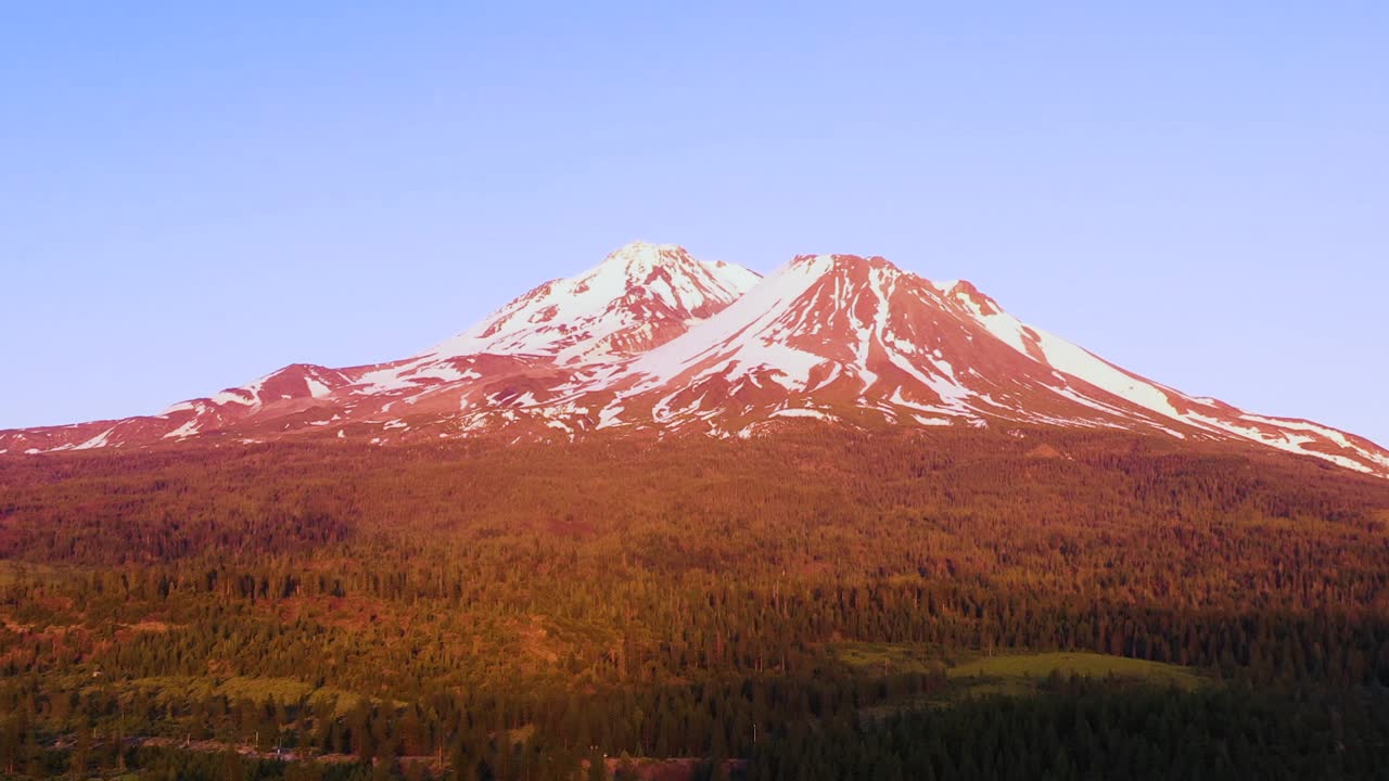 리버스 드론 샷은 캘리포니아의 마운트 샤스타를 덮고 있는 분홍색 색조를 보여줍니다.