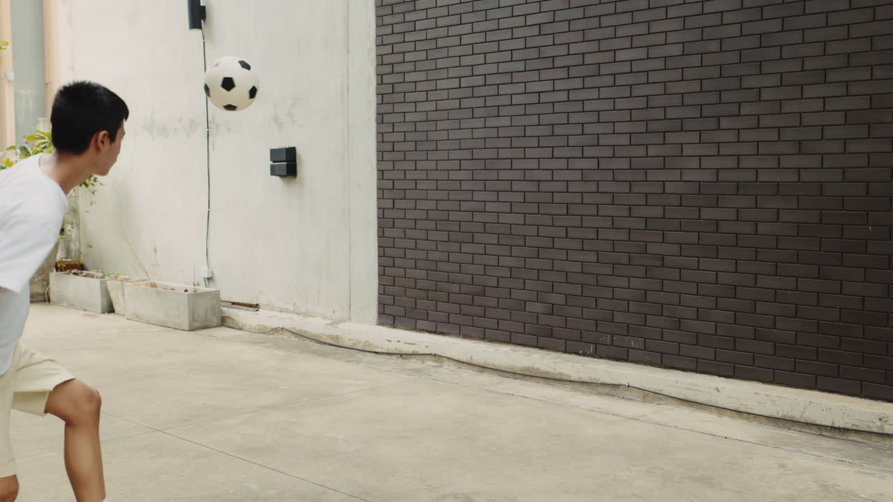 A boy playing soccer against a wall