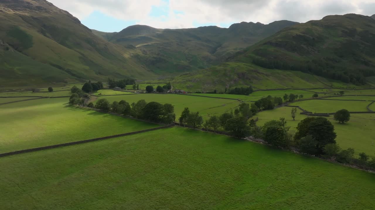 Terreni agricoli con muri in pietra in un'ampia valle con montagne scure e pozze di sole. Great Langdale. Estate. Lake District, Cumbria, Regno Unito.
