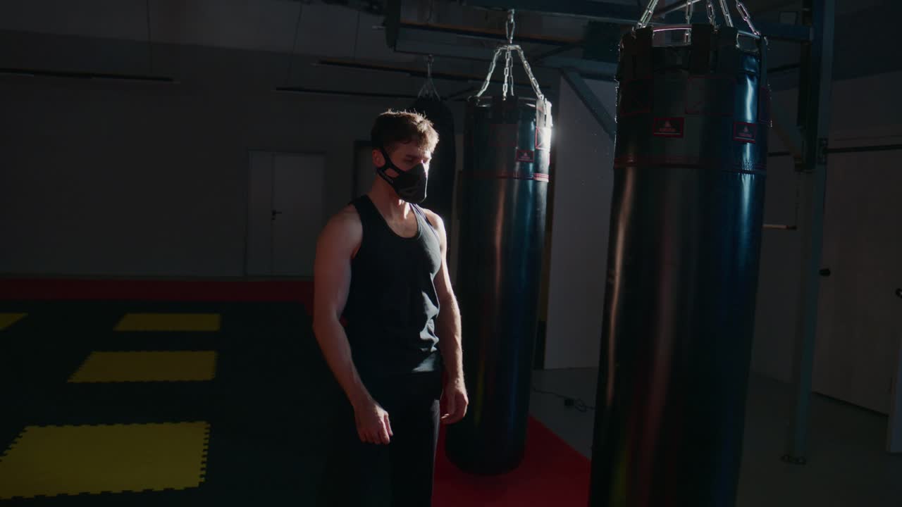 Man in Training Mask Standing in Dark Gym with Punching Bags