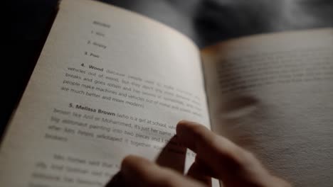 close-up of a hand turning the page of a book with text on the pages in focus, and the words clearly legible