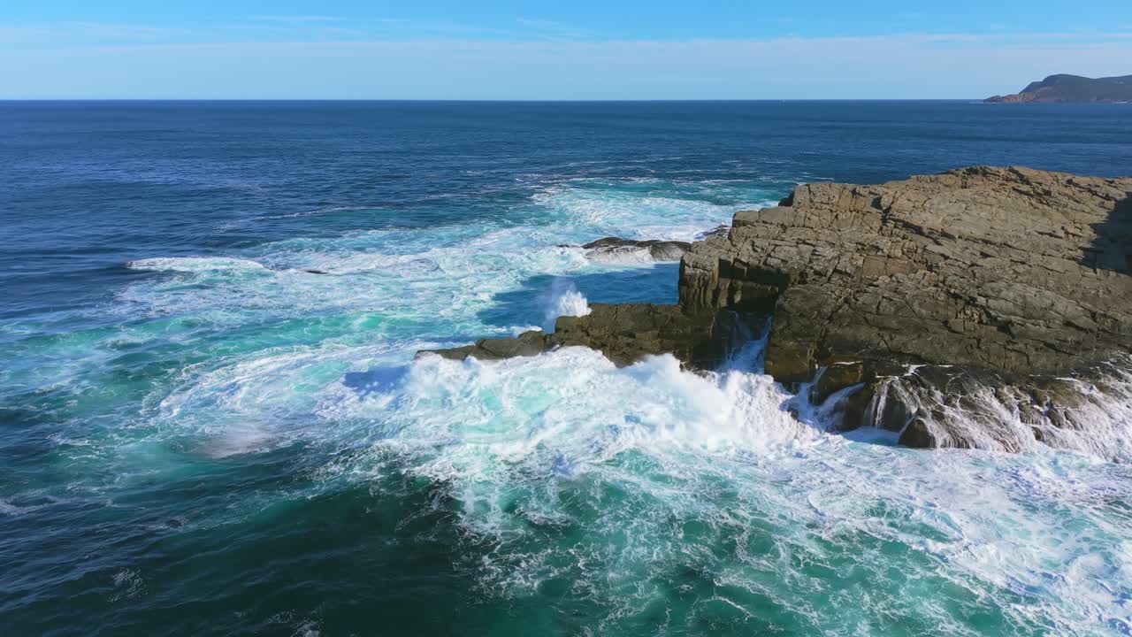 Aerial drone footage of Flatrock Beamer shows waves sweeping over a rocky peninsula and swirling turquoise water, revealing the power and beauty of Newfoundland’s Atlantic coast on a clear day