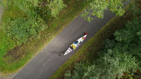 drone shot of hikers walking with canoe across a straight road in the green woods