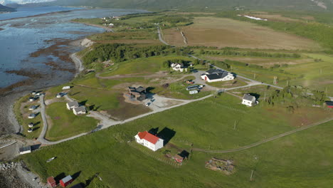 vista aérea hacia un pequeño pueblo en la costa del océano ártico, soleado, día de verano, en troms, nordland, norte de noruega - inclinación hacia abajo, disparo de drones
