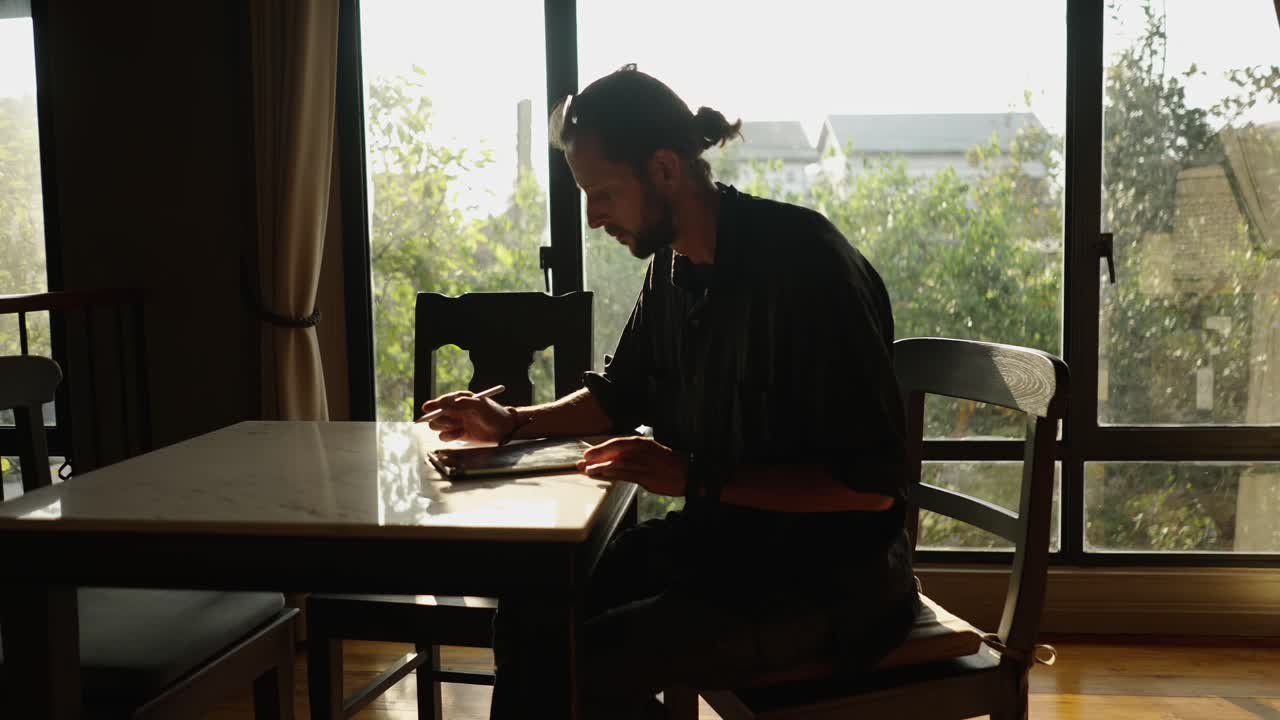 Man sitting at a table by a window using a tablet