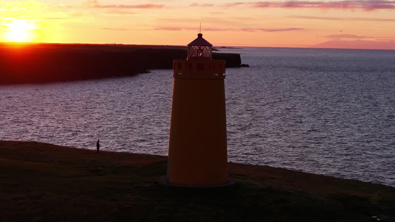 Ampia ripresa aerea di un faro giallo sulle scogliere di Keflavík con un uccello che passa nelle vicinanze.