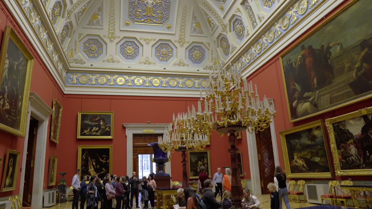 Pan down from detailed and decorated arced ceiling to a hall full of visitors and old framed paintings in Hermitage museum in St. petersburg, russia