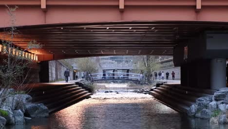 a view to a water stream under the bridge in a city in the evening