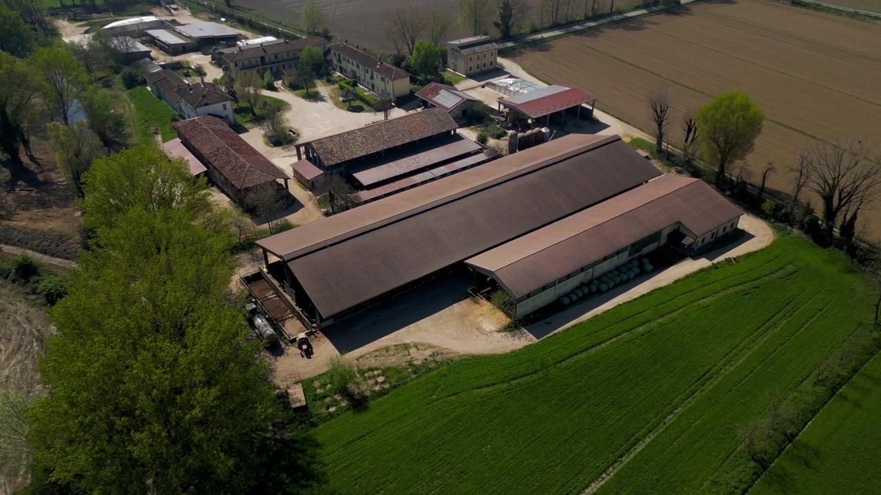 Vista aerea di un'azienda lattiero-casearia nel nord Italia. Stalle ed edifici agricoli mostrano la produzione di latte e l'attività agricola all'interno di un paesaggio rurale gestito.