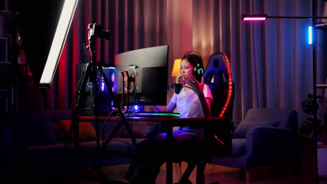 asian girl streamer playing game over network on personal computer. challenge and bully threat killing competitor, live stream video game, desk illuminated by rgb led strip light