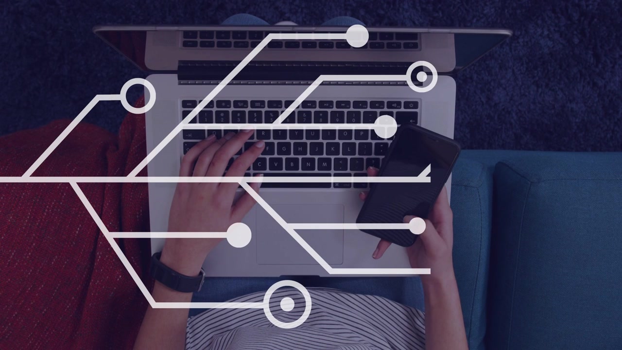 Female tech worker typing on laptop and tilting phone, causing circuit nodes growing across devices