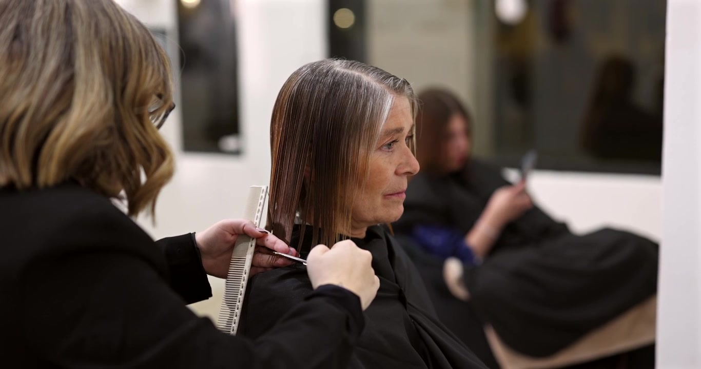Parrucchiere professionista che taglia i capelli a una donna matura in un salone