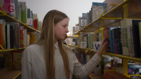 teenage girl searching for a book in library bookcases, handheld close up shot