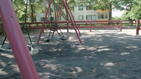 empty swings swaying at the playground with apartment building in the background