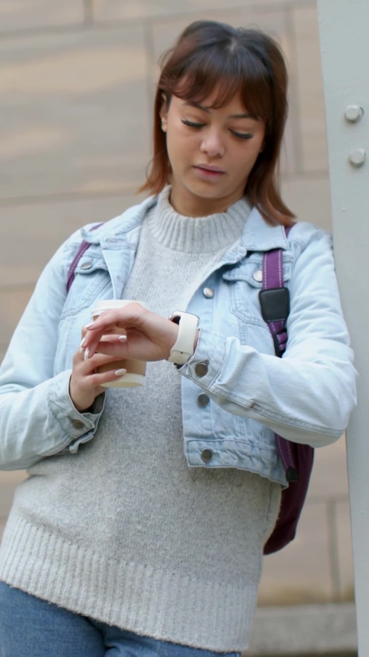 Vertical video: Scanning, woman in denim holding cup lifting lid checking watch for time by facade