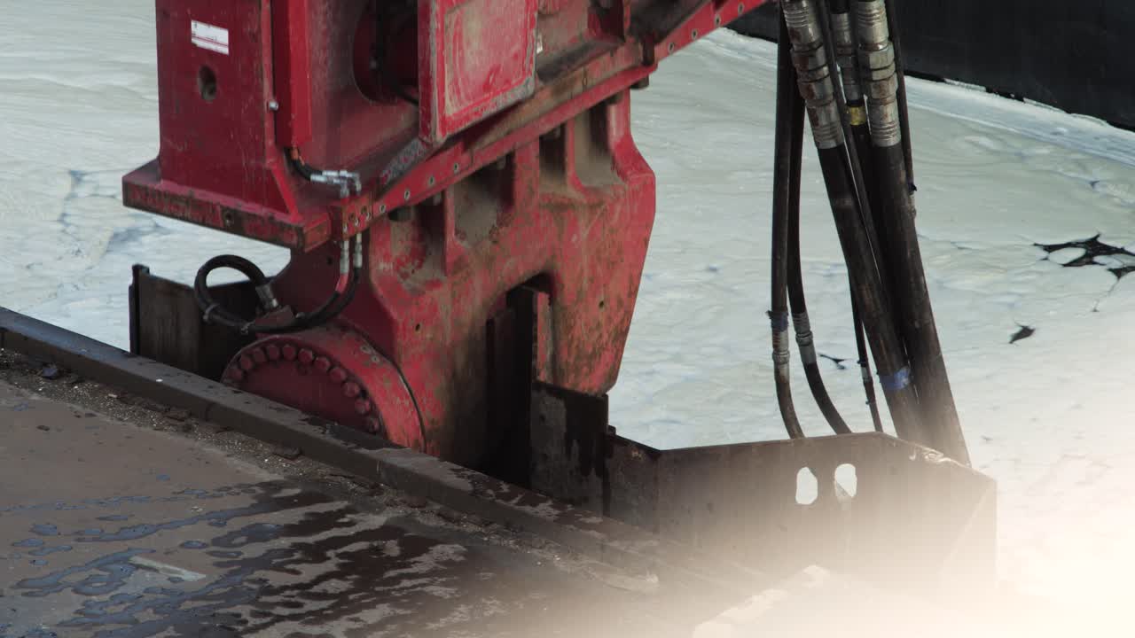 Close-up of red vibratory hammer pulling out steel sheet pile with visible vibration