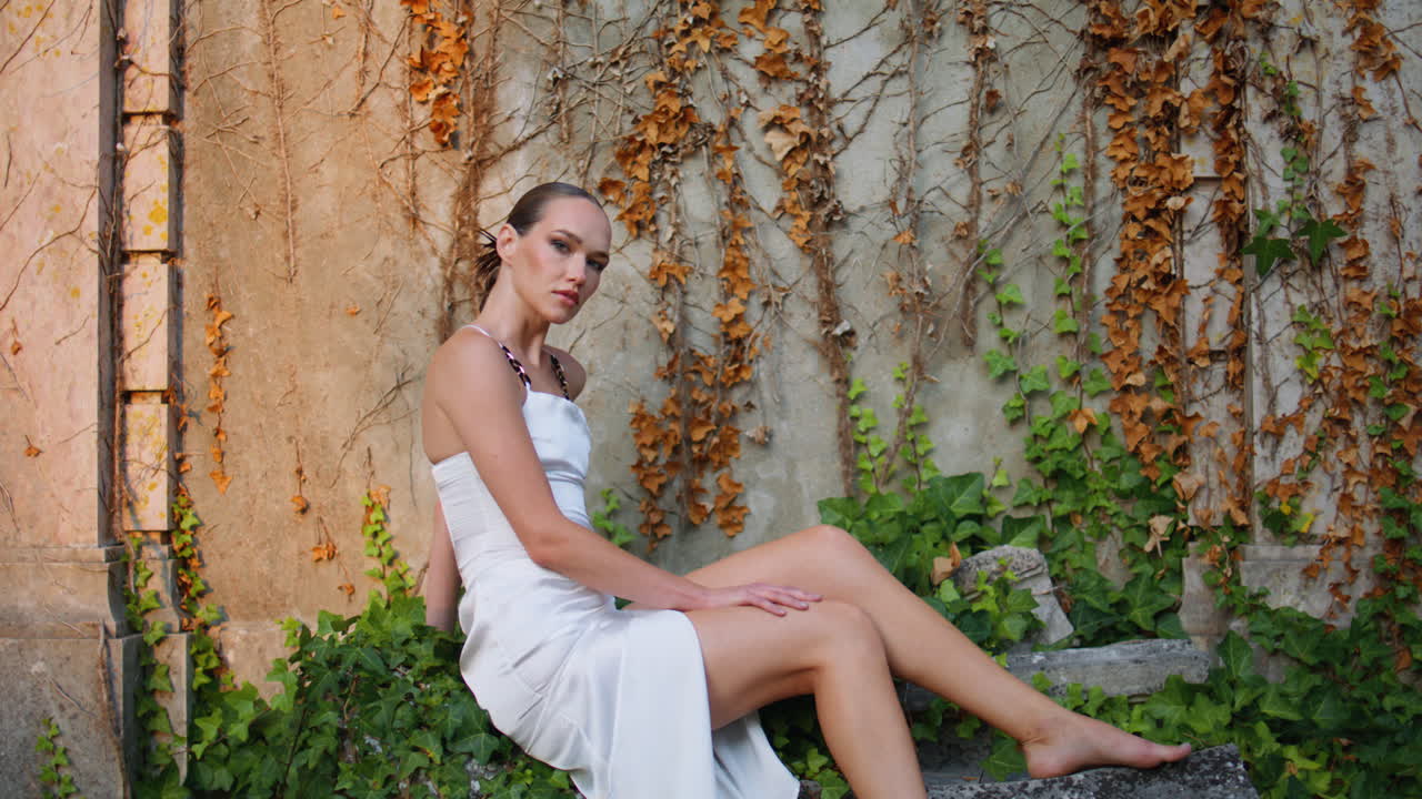 우아한 소녀가 앞에 앉아 돌 오래된 벽 인 가을 잎을 확대.