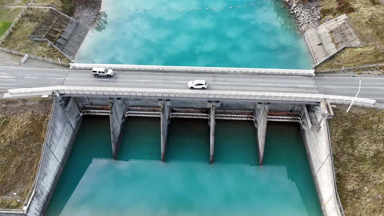Drone footage captures cars crossing a bridge over the turquoise waters of Lake Tekapo dam in New Zealand