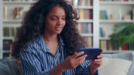Indian teenage girl holding phone while looking at screen while sitting at home