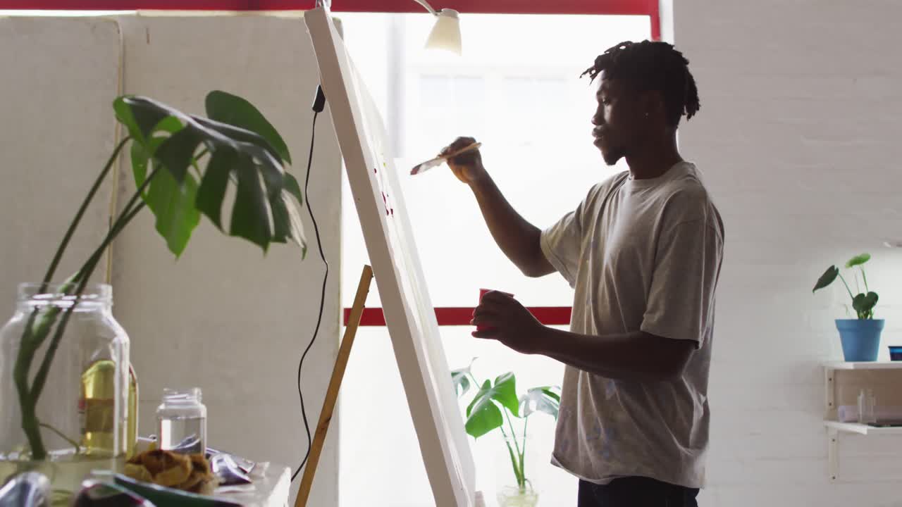 Vista laterale di un artista maschio afroamericano che dipinge su tela nello studio d'arte.