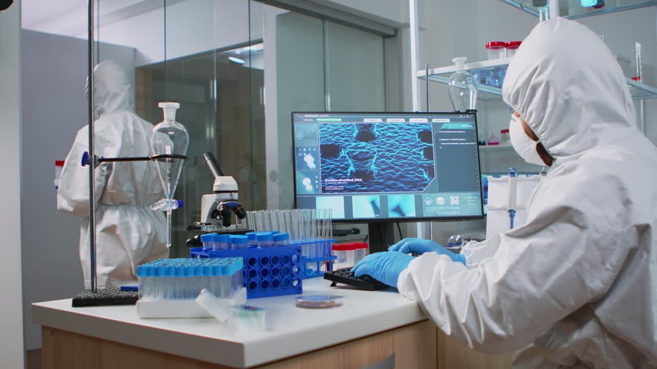 Chemist in coverall typing on computer analysing vaccine evolution