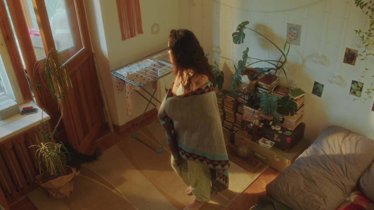 지루한 어린 소녀가 담요로 감싸서 쾌적한 빛 방을 돌아다니고 있다