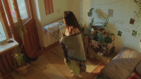 young bored girl wrapped in blanket wandering around cozy sunlit room