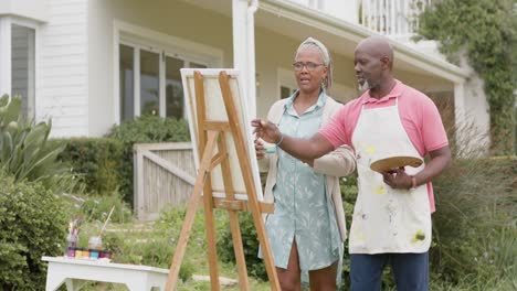 Feliz-Pareja-Afroamericana-Mayor-Pintando-Sobre-Caballete-De-Madera-En-El-Jardín,-Cámara-Lenta