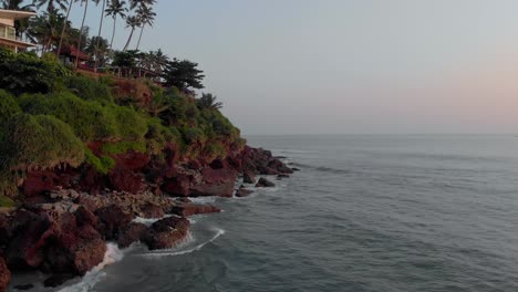 forward moving aerial along the tall dense green cliffs of varkala beach, kerala, india showing low tides hitting the rocks