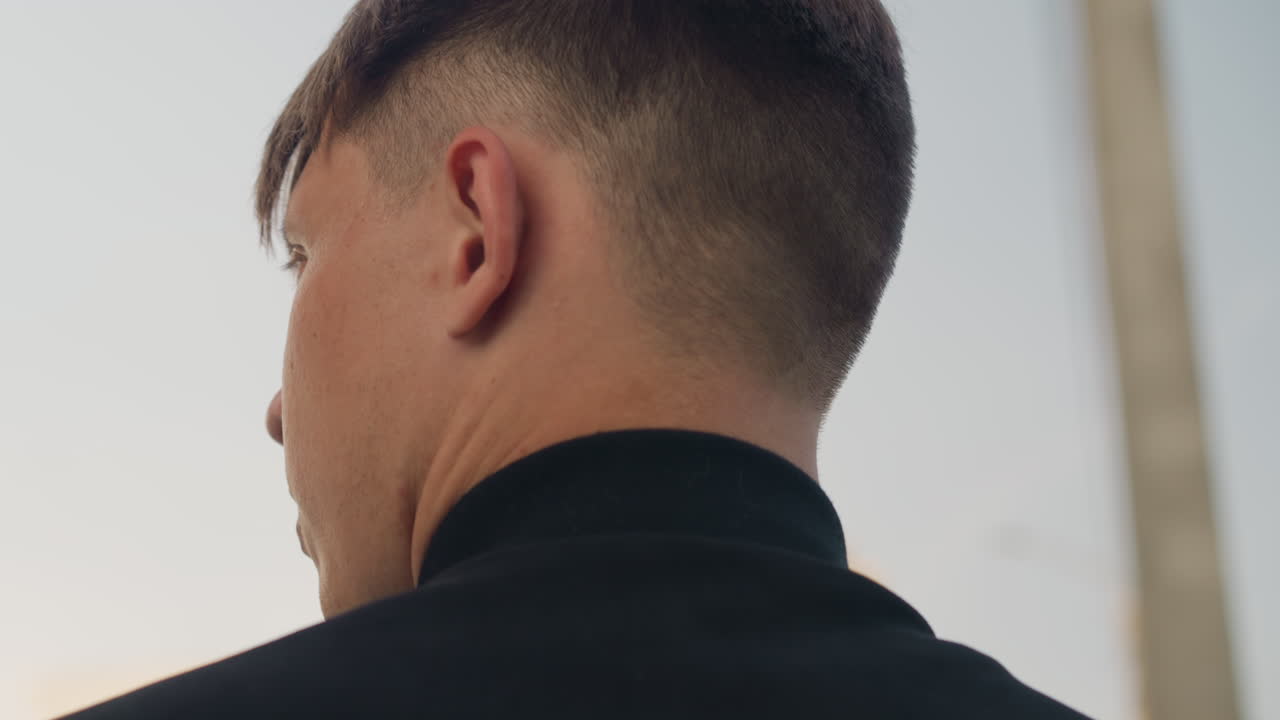 창문 밖 도시 스카이라인이 반사된 배경을 뒤로 하고, 코트 깃을 세운 채 출근하는 흰색 셔츠의 뒷모습, 차분한 아침의 분위기, 단정한 헤어스타일, 코트 깃을 올림, 조용한 일상과 도시의 통근 분위기