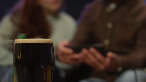 close up of pint of stout with friends at home or in bar celebrating at st patrick's day party posing for selfie in background