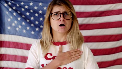 una joven rubia canta frente a la bandera estadounidense.