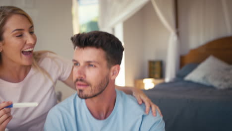pareja emocionada en el dormitorio en casa celebrando el resultado positivo de la prueba de embarazo