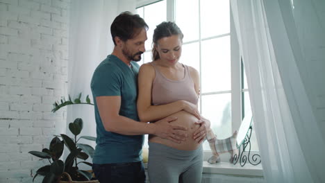 happy husband holding belly og pregnant wife at home. pregnant couple hugging