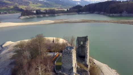 Avance-Aéreo-Sobre-El-Lago-Gruyere-Con-Ruinas-Del-Castillo-De-Pont-En-Ogoz-En-La-Isla-De-Oiseaux