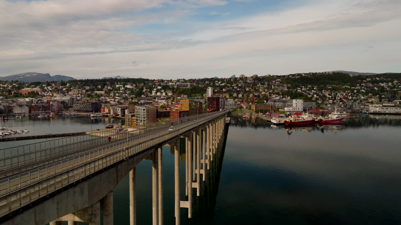 Ponte di Tromso, Norvegia, che attraversa acque calme verso il lungomare e il porto della città sotto una morbida luce estiva, veduta aerea cinematografica.