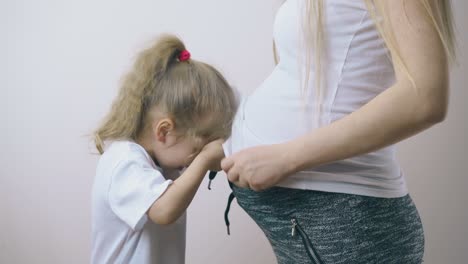 la niña trata de esconderse debajo de la camiseta de la madre embarazada