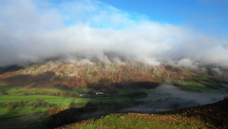 sunlit hillside with flight towards green valley and cloud shrouded mountains lit by early morning autumn sunshine