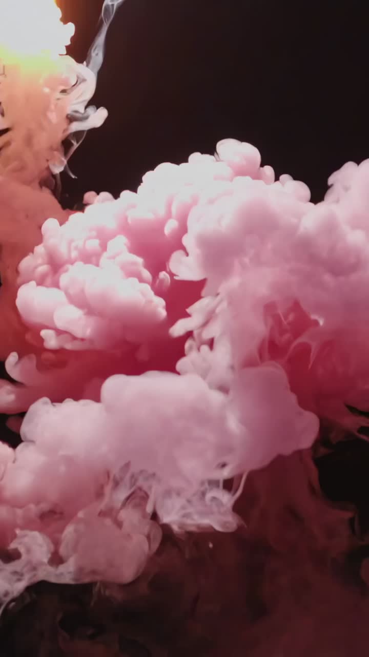 Video verticale: goccia che entra nel serbatoio, pennacchio rosa che si gonfia in tenui volute su uno sfondo nero illuminato in studio