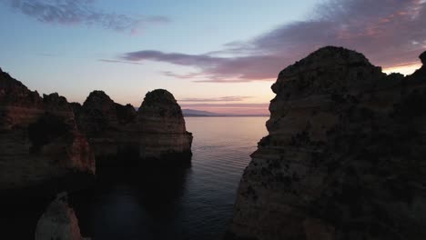 drone flying between rock formations along portugal's coast, at sunrise, golden hour