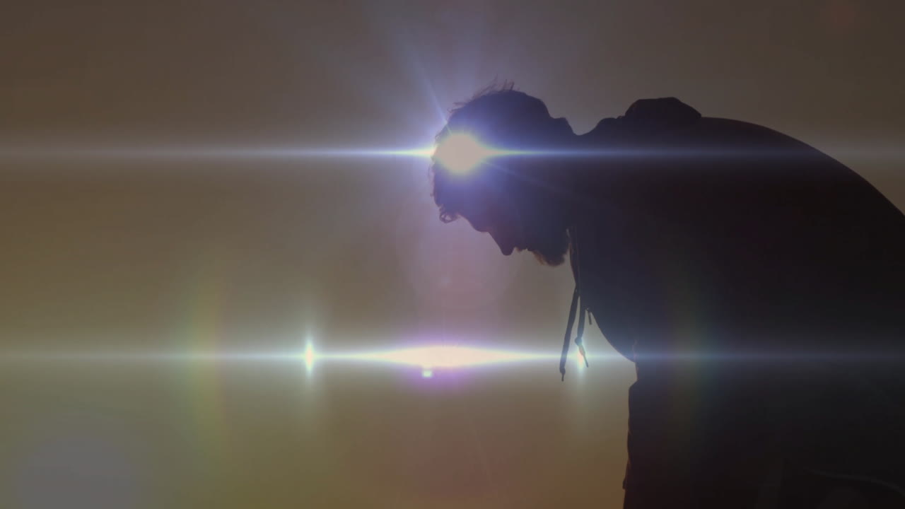 Bending forward, person in silhouette with bright light flares behind