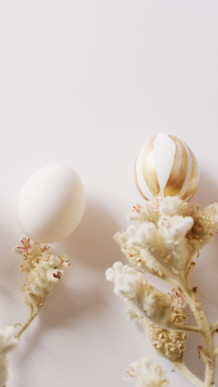 Vertical video of easter eggs with flowers on white background with copy space