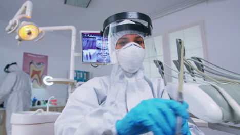 Patient-pov-of-dentist-holding-dental-tools-wearing-covid-protection-suit