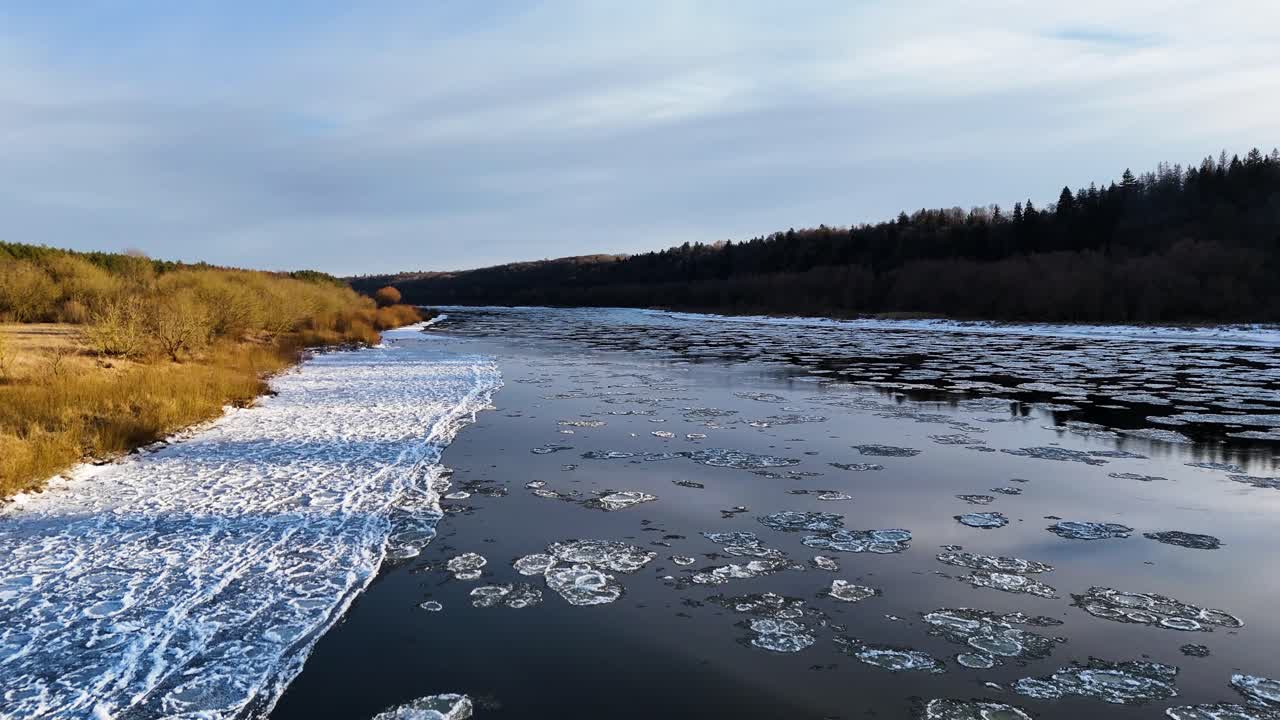 Sky reflecting on calm river with flowing ice, aerial view