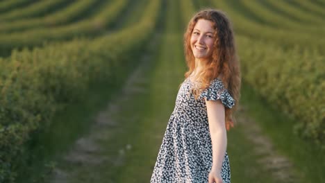 beautiful young woman with red hair in a dress runs across the field and looks around at the camera