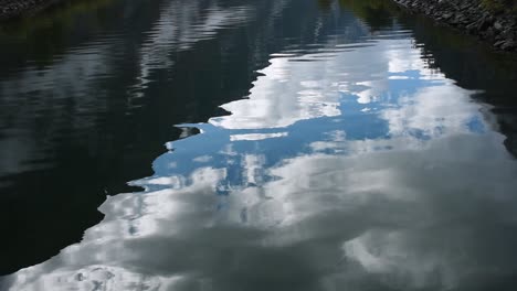 Vista-De-Cerca-De-Una-Superficie-De-Agua-Mágica-Que-Refleja-Un-Cielo-Azul-Con-Nubes-En-Ondas-Suaves