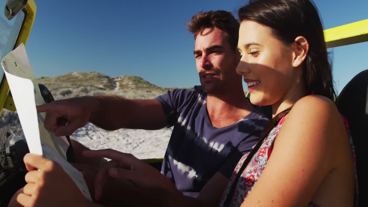 pareja caucásica sentada en un buggy de playa junto al mar leyendo un mapa