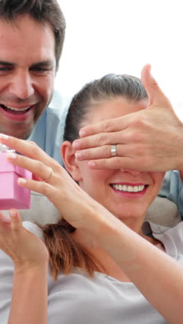 hombre sorprendiendo a su novia con un regalo rosa en el sofá