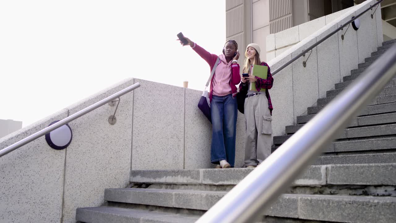 Diverse female pals on stairs greeting arrival checking phones green folder taking selfie