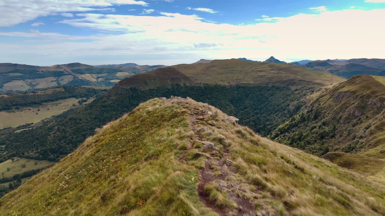 Movimento aereo sopra una dorsale erbosa che rivela vette e valli distanti. Topografia panoramica della regione dell'Alvernia
